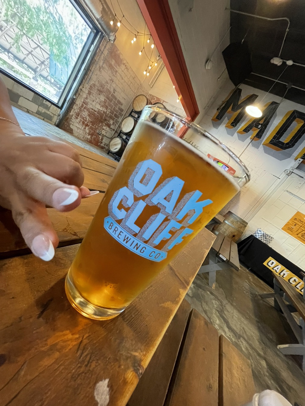 A golden Chico lager in an Oak Cliff Brewing pint glass on a wooden taproom table.